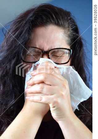 Woman blowing her nose hard into a tissue at home 39828016