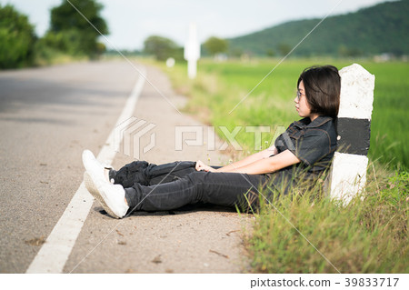 Woman sit with backpack hitchhiking along a road in countryside Woman sit with backpack hitchhiking along a road in countryside 39833717