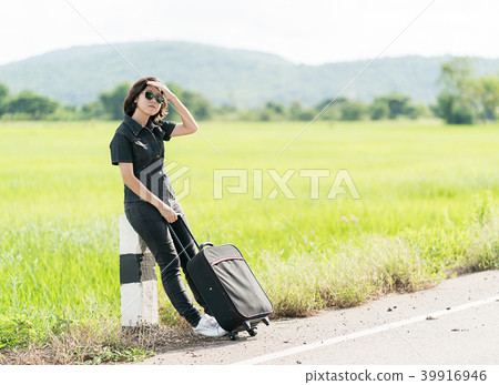 Woman with luggage hitchhiking along a road Woman with luggage hitchhiking along a road 39916946