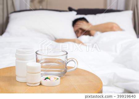 man on bed with medicine, drugs and glass of water 39919640