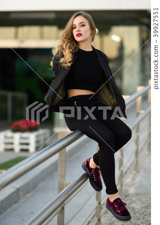 Beautiful young girl wearing black jacket sitting in the street. 39927551