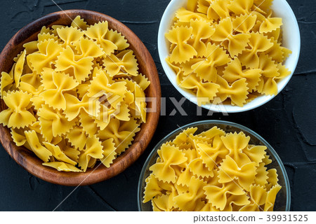 farfalle macaroni Wooden white and glass bowl with pasta on a textured black background, close-up farfalle macaroni Wooden white and glass bowl with pasta on a textured black background, close-up 39931525