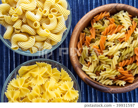Multicolor spiral macaroni Wooden white and glass bowl with pasta on a textured blue white striped 39931597
