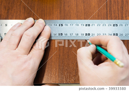 Close-up Men's hands draw a pencil on the ruler with a sub-standard template for cutting out Close-up Men's hands draw a pencil on the ruler with a sub-standard template for cutting out 39933380