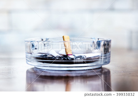 Cigarette butts and ashes in a glass ashtray. 39933832