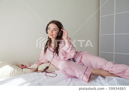brunette in pink Pajamas listening to music with headphones on the bed 39934865