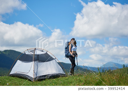 Woman tourist near camping in the mountains with backpack and trekking sticks in the morning 39952414
