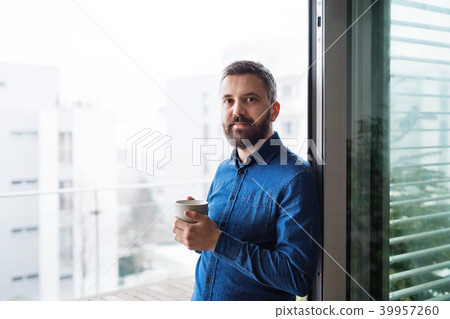 A man by the window holding a cup of coffee at home. A man by the window holding a cup of coffee at home. 39957260