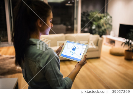 A woman holding a tablet with smart home screen. 39957269