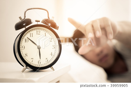 Man hand reaching out to alarm clock for snooze Man hand reaching out to alarm clock for snooze 39959905
