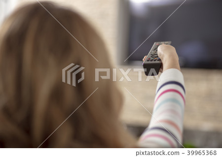 Beautiful woman lying on a sofa with remote control and watching television Beautiful woman lying on a sofa with remote control and watching television 39965368