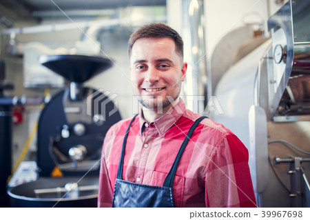 Portrait of young man in apron on background of industrial coffee grinder Portrait of young man in apron on background of industrial coffee grinder 39967698