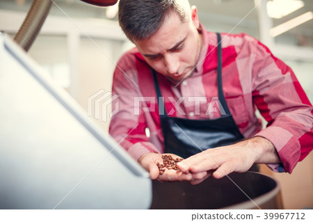 Image of young businessman with coffee beans in hand next to roaster 39967712