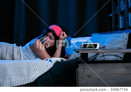 Image of young brunette with insomnia with pink eye patch lying on bed next to clock Image of young brunette with insomnia with pink eye patch lying on bed next to clock 39967736