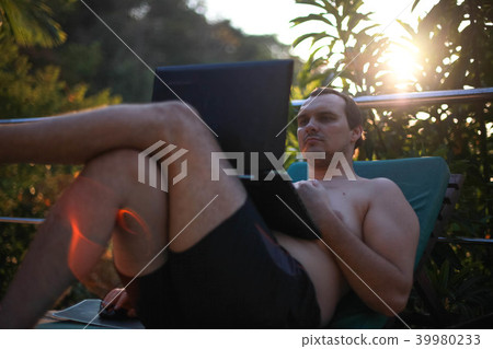 Man working on laptop by swimming-pool during sunset in tropical jungle Man working on laptop by swimming-pool during sunset in tropical jungle 39980233