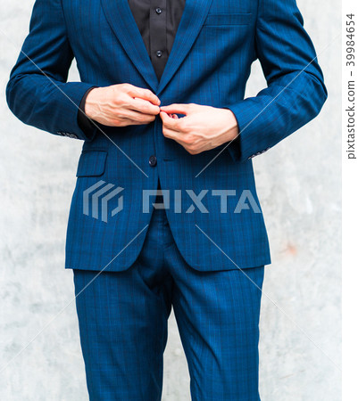 A man wearing a suit in front of a wall. 39984654