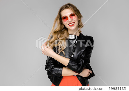 Attractive young blonde girl in striped blouse and leather jacket smiling in sunglasses with hands Attractive young blonde girl in striped blouse and leather jacket smiling in sunglasses with hands 39985185