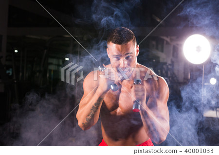 Powerful man doing boxing exercises, making direct hit with dumbbells. Photo of sporty muscular male Powerful man doing boxing exercises, making direct hit with dumbbells. Photo of sporty muscular male 40001033