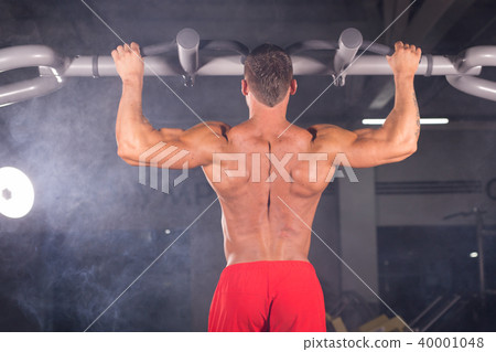 Athlete muscular fitness male model pulling up on horizontal bar in a gym. Athlete muscular fitness male model pulling up on horizontal bar in a gym. 40001048