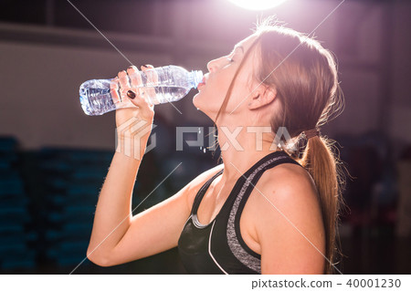 Side view of beautiful girl in sport clothes drinking water after workout in gym 40001230