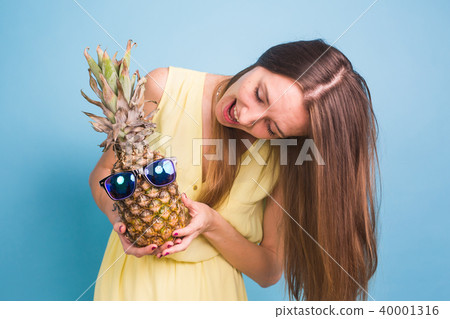 Portrait smiling woman and pineapple in sunglasses over blue background. Summer concept Portrait smiling woman and pineapple in sunglasses over blue background. Summer concept 40001316