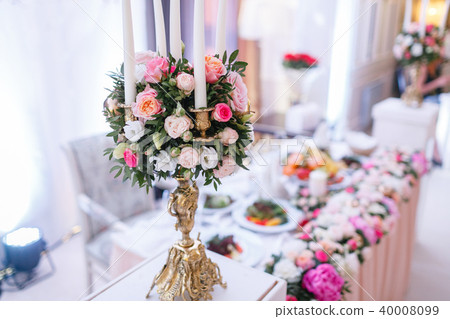 White candles on metal gold chandelier stand on tables at luxury wedding reception in restaurant 40008099