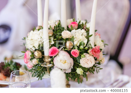 White candles on metal gold chandelier stand on tables at luxury wedding reception in restaurant 40008135