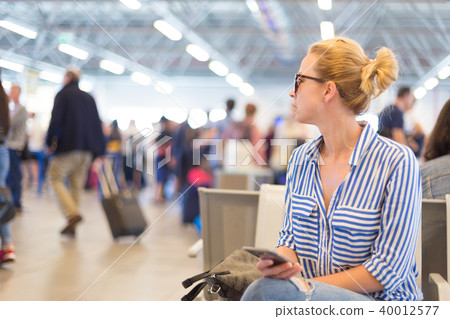 Woman using her cell phone while waiting to board a plane at departure gates at international 40012577