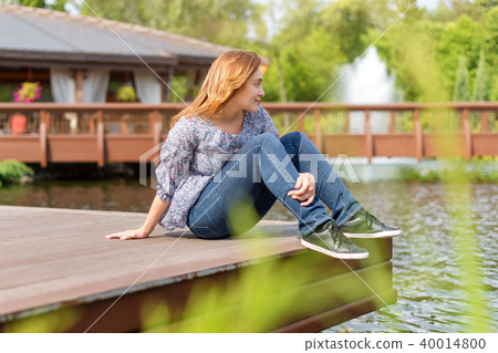 Young woman resting and having fun in the park sitting on a pier over the lake. Young woman resting and having fun in the park sitting on a pier over the lake. 40014800