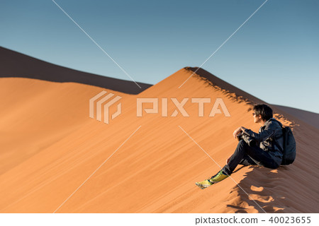 male photographer sitting on sand dune, Namibia 40023655