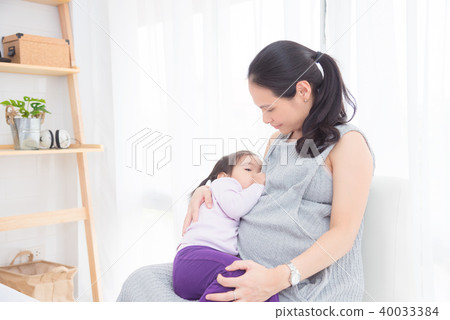Pregnant mother breast feeding her daughter  40033384