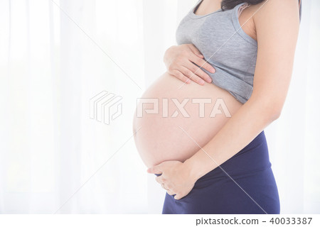 pregnant woman holding belly in front of window 40033387
