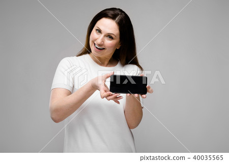 Emotional smiling happy plus size model standing in studio looking in camera offering mobile phone Emotional smiling happy plus size model standing in studio looking in camera offering mobile phone 40035565
