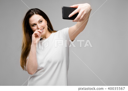 Emotional smiling happy plus size model standing in studio looking in camera making selfie Emotional smiling happy plus size model standing in studio looking in camera making selfie 40035567