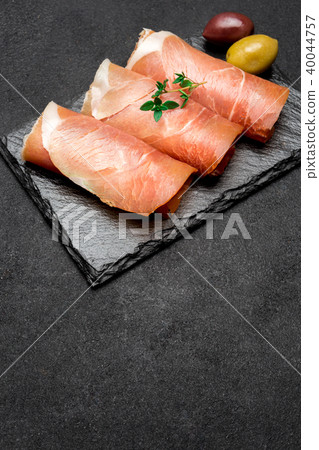 proscuitto ham arranged in thinly sliced rolls on stone serving board 40044757