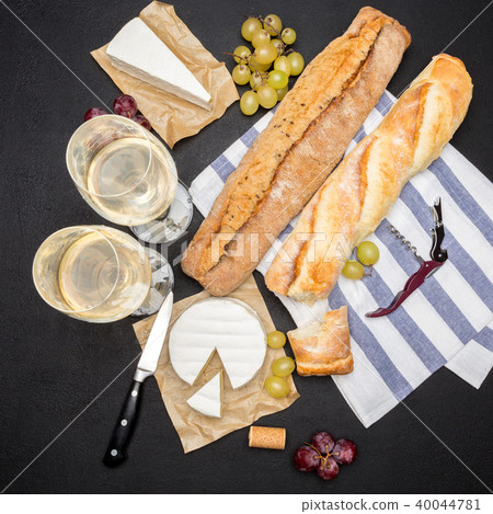 brie cheese, baguette and two glasses of white wine on dark concrete background 40044781