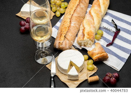 brie cheese, baguette and two glasses of white wine on dark concrete background brie cheese, baguette and two glasses of white wine on dark concrete background 40044783