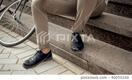 Closeup photo of male feet sitting on stone stairs next to bicycle 40050288