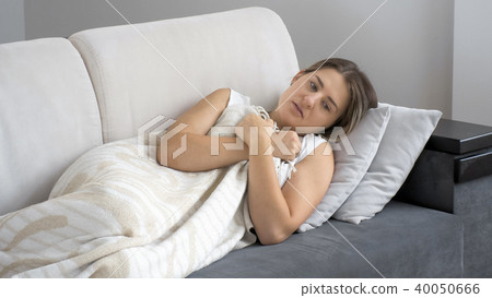 Young ill brunette woman feeling cold while lying under blanket on sofa Young ill brunette woman feeling cold while lying under blanket on sofa 40050666