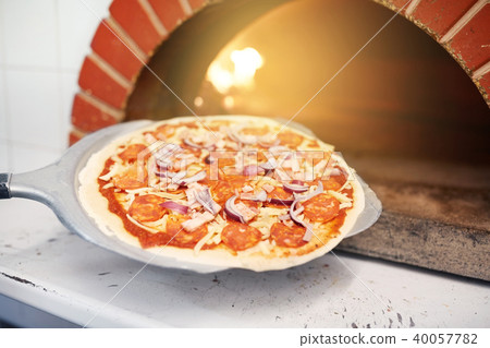 peel placing pizza into oven at pizzeria 40057782