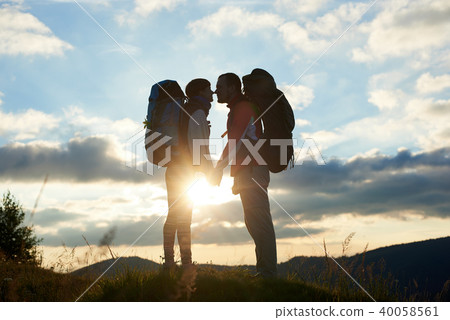Couple of tourists in love with backpacks facing each other at sunset in the mountains Couple of tourists in love with backpacks facing each other at sunset in the mountains 40058561