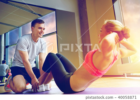 woman with personal trainer doing sit ups in gym 40058871