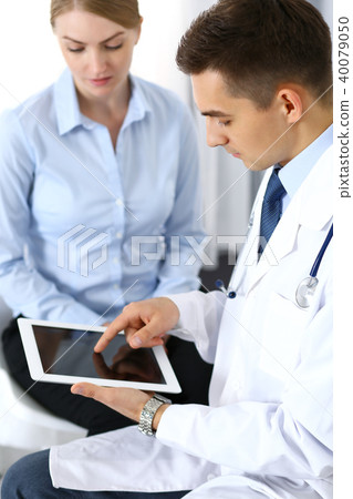 Male doctor using touchpad or tablet pc while consulting female patient in hospital office. Medicine 40079050