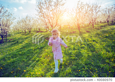 Little baby girl that runs between flowering trees at sunset. Ar Little baby girl that runs between flowering trees at sunset. Ar 40080970