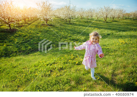 Little baby girl that runs between flowering trees at sunset. Ar Little baby girl that runs between flowering trees at sunset. Ar 40080974