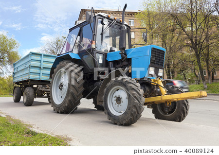 An old small blue tractor with a trailer stands An old small blue tractor with a trailer stands 40089124