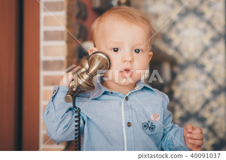 A little blond boy in a blue shirt is calling on the phone A little blond boy in a blue shirt is calling on the phone 40091037