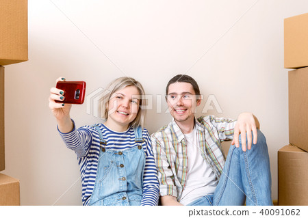 Photo of young married couple doing selfie sitting on floor among cardboard boxes Photo of young married couple doing selfie sitting on floor among cardboard boxes 40091062