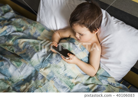 modern boy playing phone lying on the bed in morning modern boy playing phone lying on the bed in morning 40106083