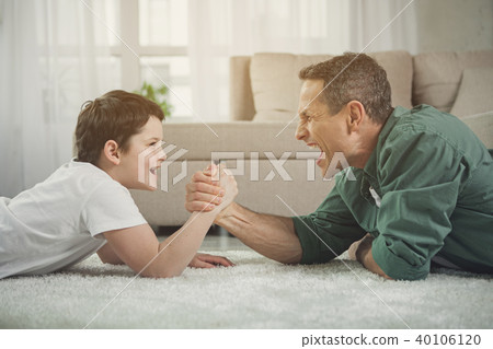 Cheerful father and son playing arm-wrestling at home Cheerful father and son playing arm-wrestling at home 40106120